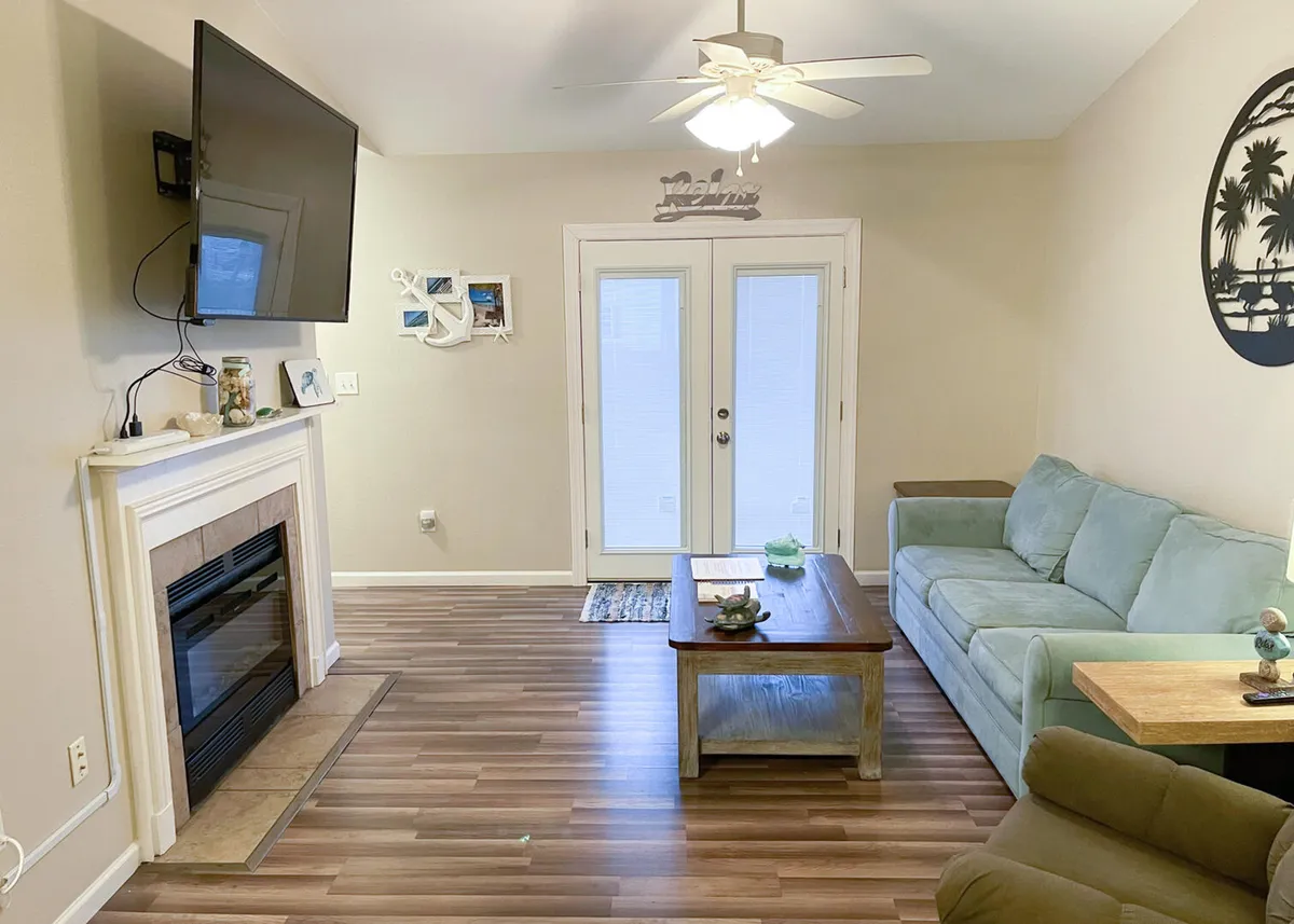A tastefully furnished living room with a plush sofa, coffee table, and a fireplace, set against double doors that let in natural light. The arrangement suggests a warm, inviting space ideal for gatherings, conversations, or cozy nights in.