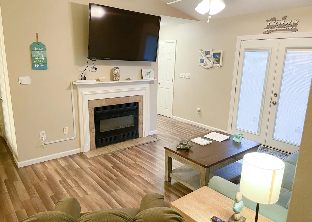 A bright, open living room featuring a comfortable sofa, a modern coffee table, a flat-screen television, and sliding glass doors that lead out to a private balcony. The space is designed for relaxation and entertainment, with ample natural light streaming in.