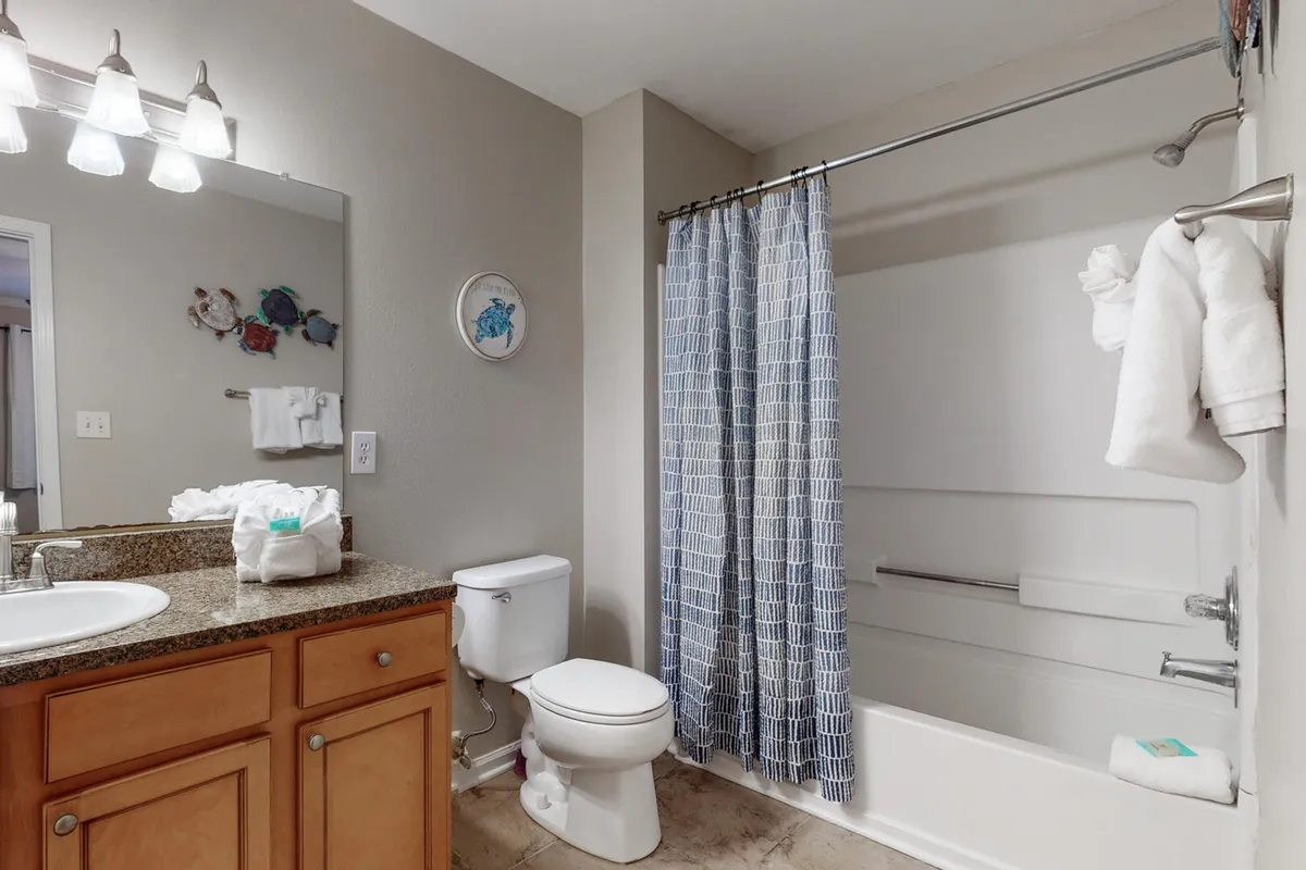 A bathroom view with a granite countertop, blue and white shower curtain, and tasteful wall art. The space feels bright, tranquil, and meticulously maintained, ideal for personal routines and relaxation.