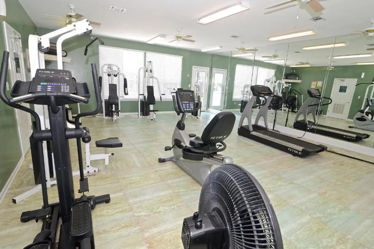 This interior image showcases a fitness center with a recumbent exercise bike, treadmills, weight machines, and a large wall mirror, creating a motivating, energetic atmosphere for residents.