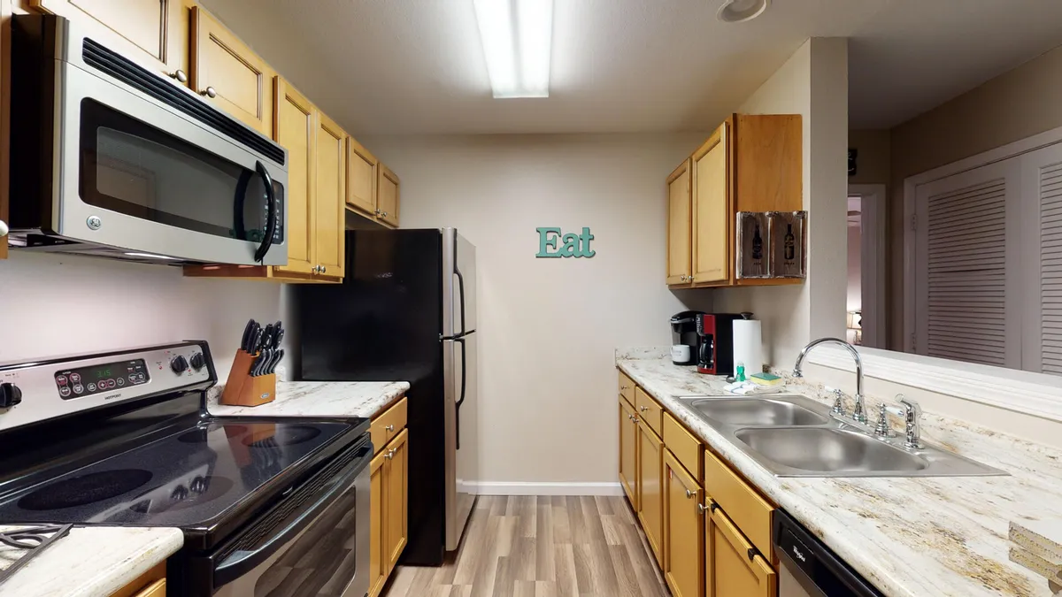 A sleek, modern kitchen with a stainless steel microwave, black refrigerator, electric stove with glass cooktop, and a double sink with chrome faucet. The space is functional, bright, and equipped for preparing anything from snacks to full dinners.