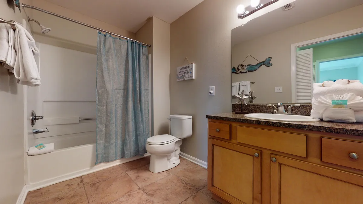 A modern, tidy bathroom featuring a bathtub with a blue shower curtain, a wooden vanity with a granite countertop and sink, a large mirror, and neatly organized fixtures. The bathroom is fresh and inviting, supporting a clean and hygienic environment.
