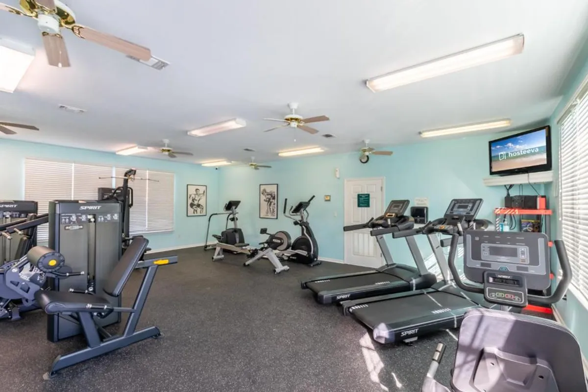 A modern, well-lit fitness center featuring treadmills, stationary bikes, weight machines, and a wall-mounted TV. The space is clean and inviting, ideal for individual workouts or social fitness sessions.