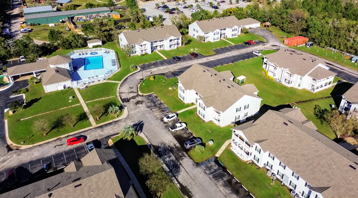 This exterior shot captures the outdoor swimming pool with an adjacent hot tub, white residential buildings with beige roofs, well-maintained green lawns, walking paths, and nearby parking. The scene is tranquil, inviting, and highlights the property's key amenities.